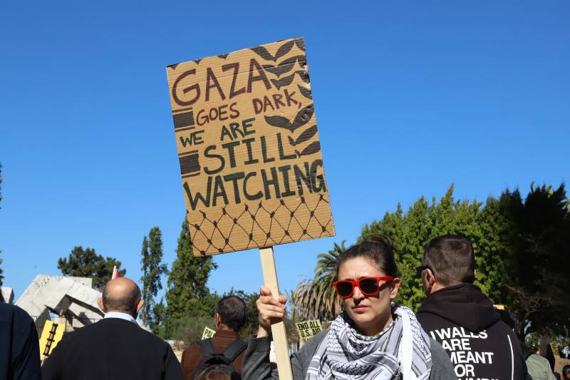 A woman stands with a sign saying: '‘Stop the Genocide in a Gaza’