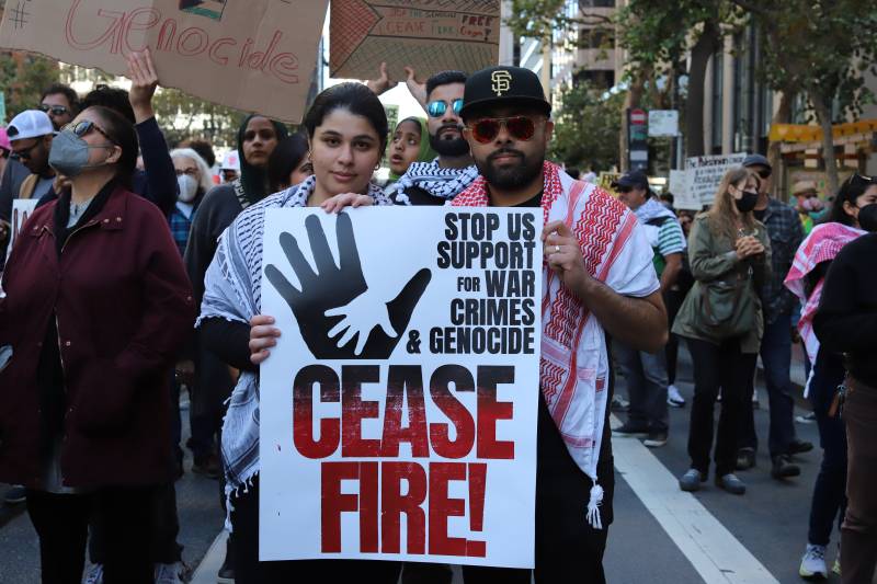 Two people stand holding a sign that says 'ceasefire.'