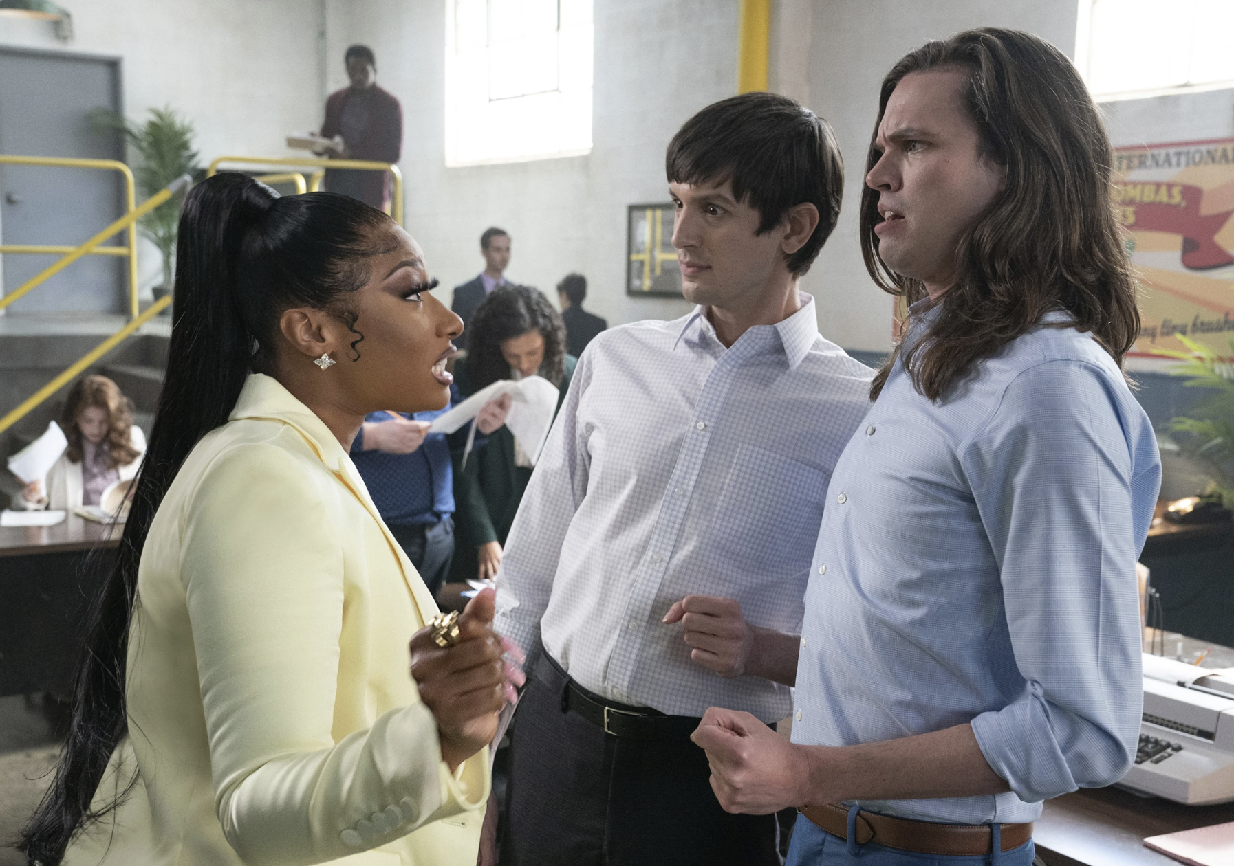 A Black woman wearing a pale yellow business suit leans in and admonishes two shocked looking white men wearing button down shirts and pants.
