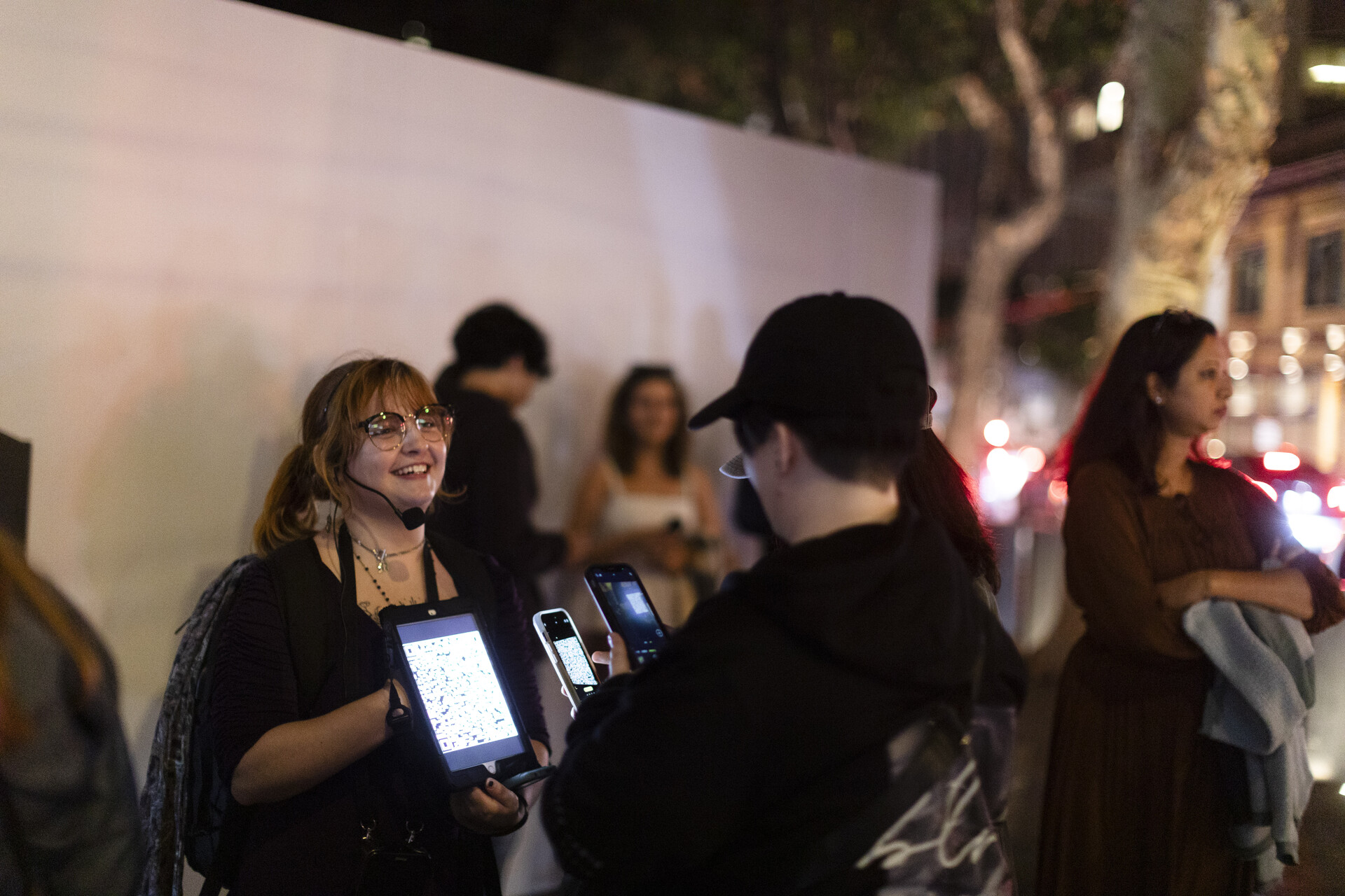 A ghost tour guide wearing a microphone holds up an iPad in front of a guest.