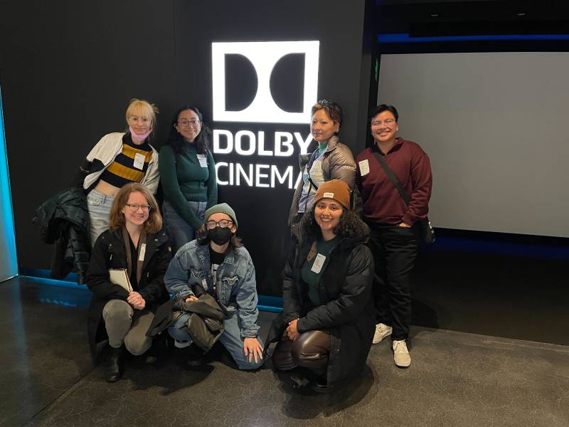 a group of seven young women pose in front of a sign that reads 'Dolby Cinema'