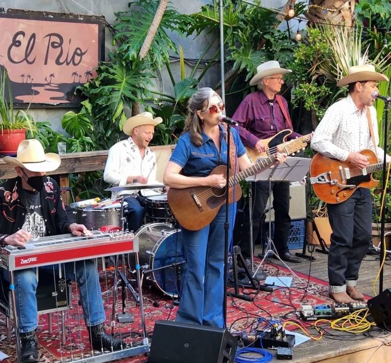 a band of five people, most of them in cowboy hats, performs on an outdoor stage at El Rio, a bar in the Mission District of San Francisco