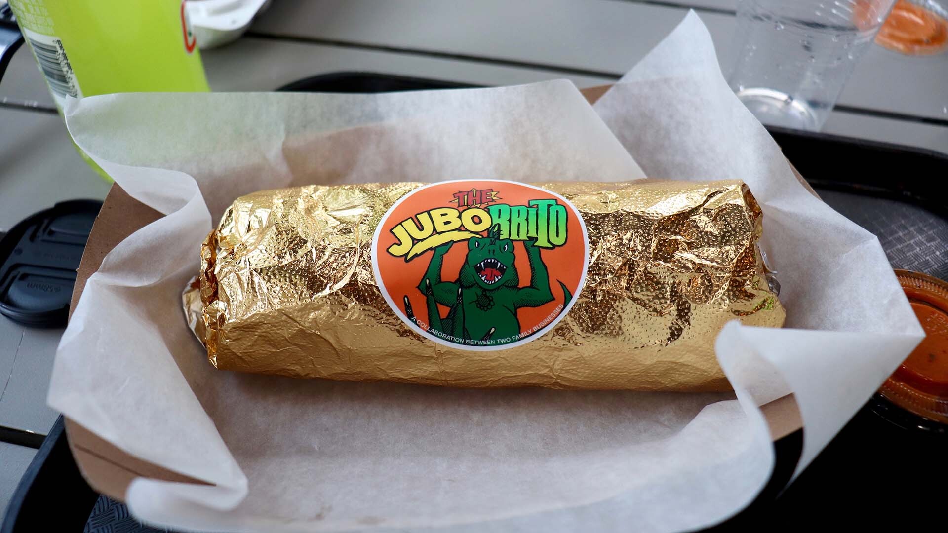 a gold-foil wrapped burrito is displayed on an outdoor table