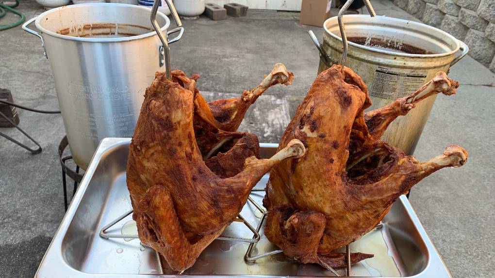 Two fried turkeys rest outdoors on a metal tray next to the large pots in which they were cooked.