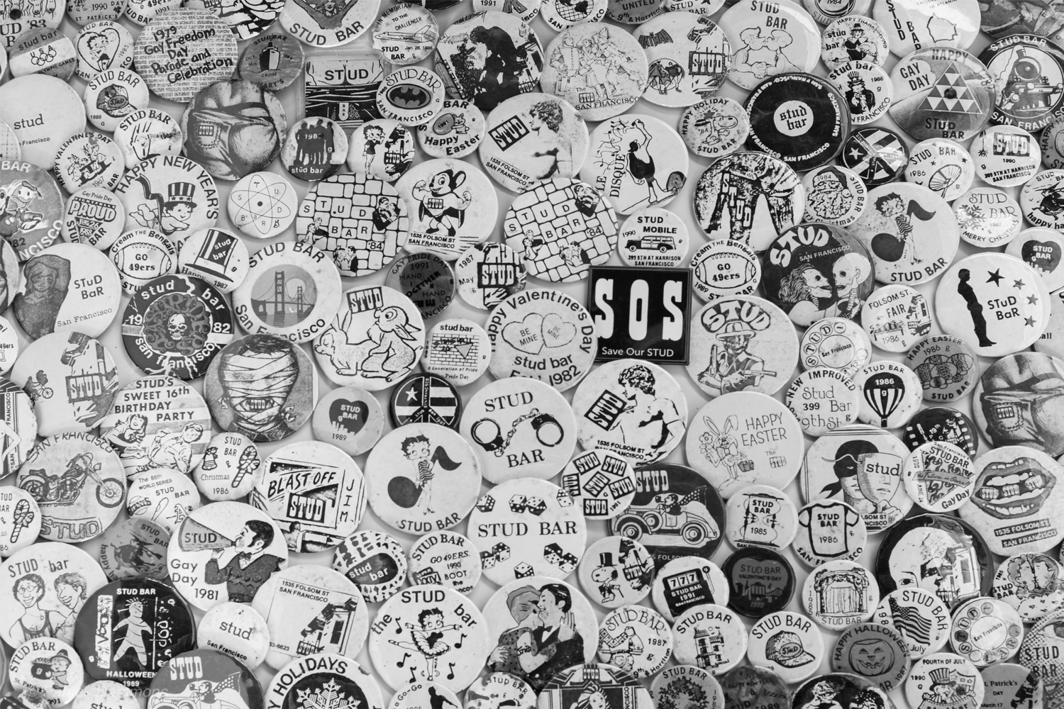 Black and white image of crowded sea of round pins with graphics advertising parties or the bar