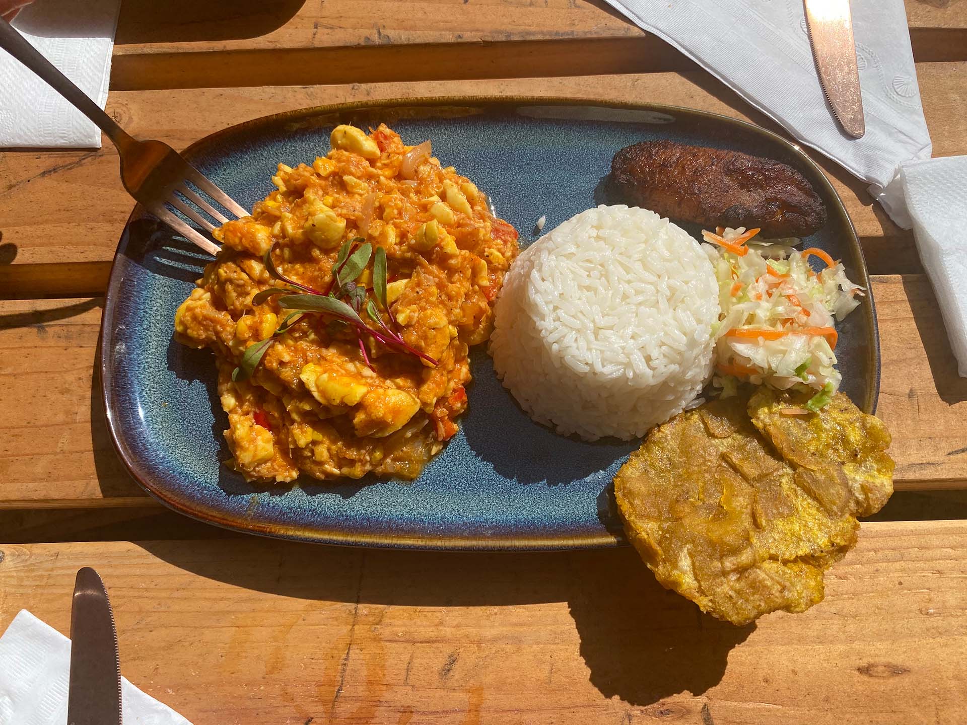Saltfish and ackee: a scramble of ackee fruit (which looks like scrambled eggs) served on a blue plate with white rice, plantains and pikliz.