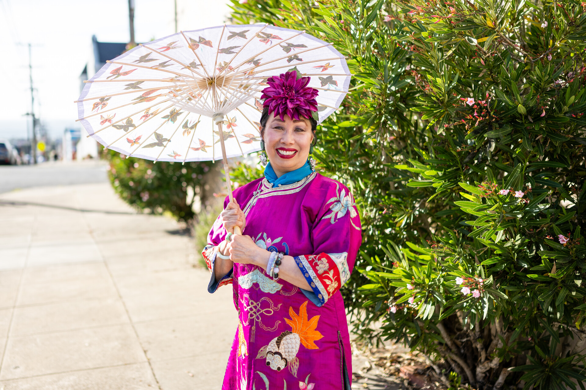Asian woman in fuchsia flowered hat holds parasol and smiles