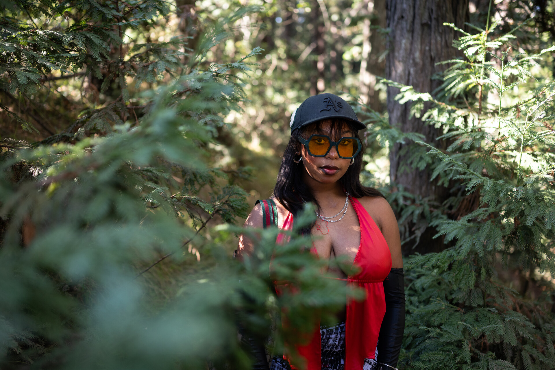 Black woman in black A's cap and red top stands among trees