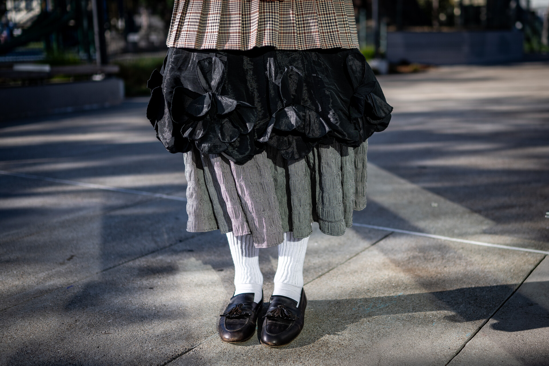 Legs-down shot of layers of gray, black and gray skirts with white socks and black loafters