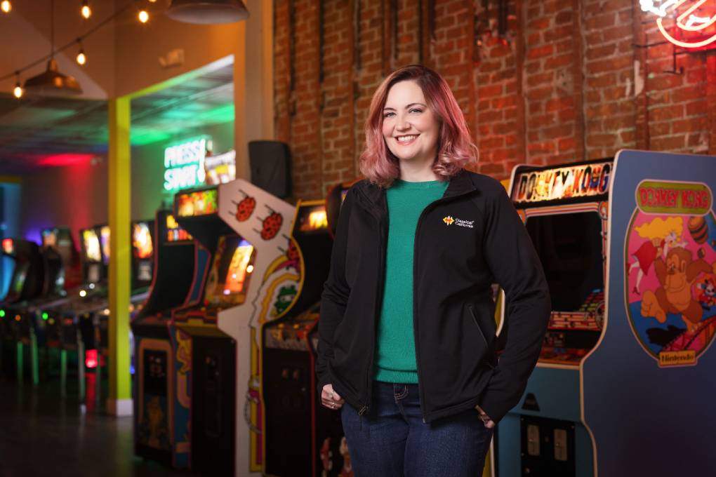 White woman smiles in an arcade in front of game consoles