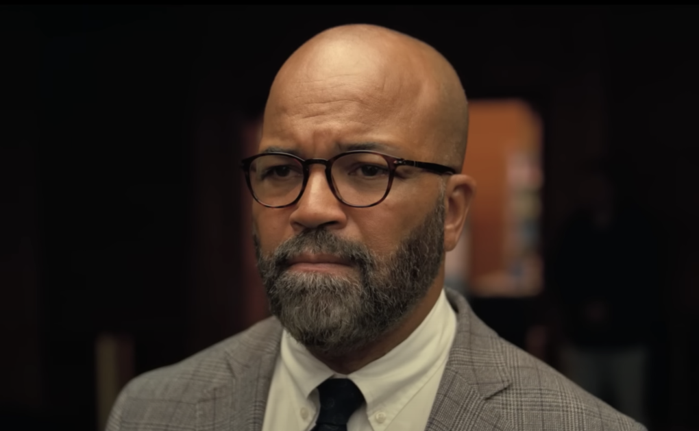 Close up on the head and shoulders of a bald, middle aged Black man with tidy, trimmed beard and round spectacles. He is wearing a white shirt, dark tie and a grey suit jacket.