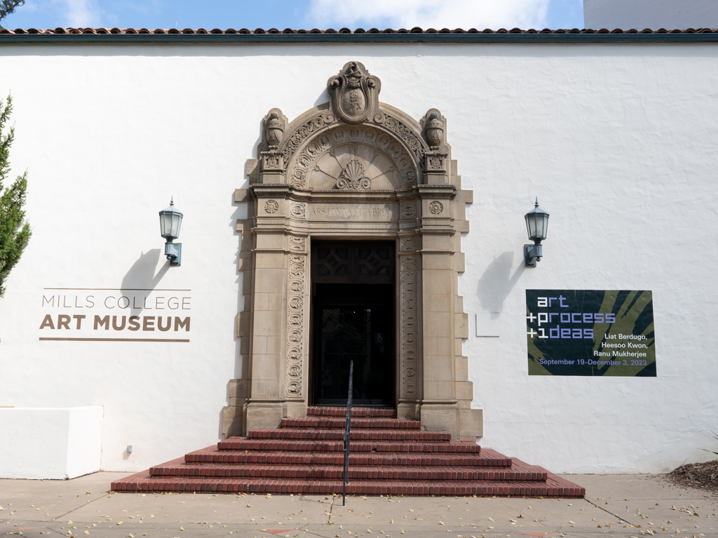 White building with ornate entrance and a tiled roof bears signs for museum and show