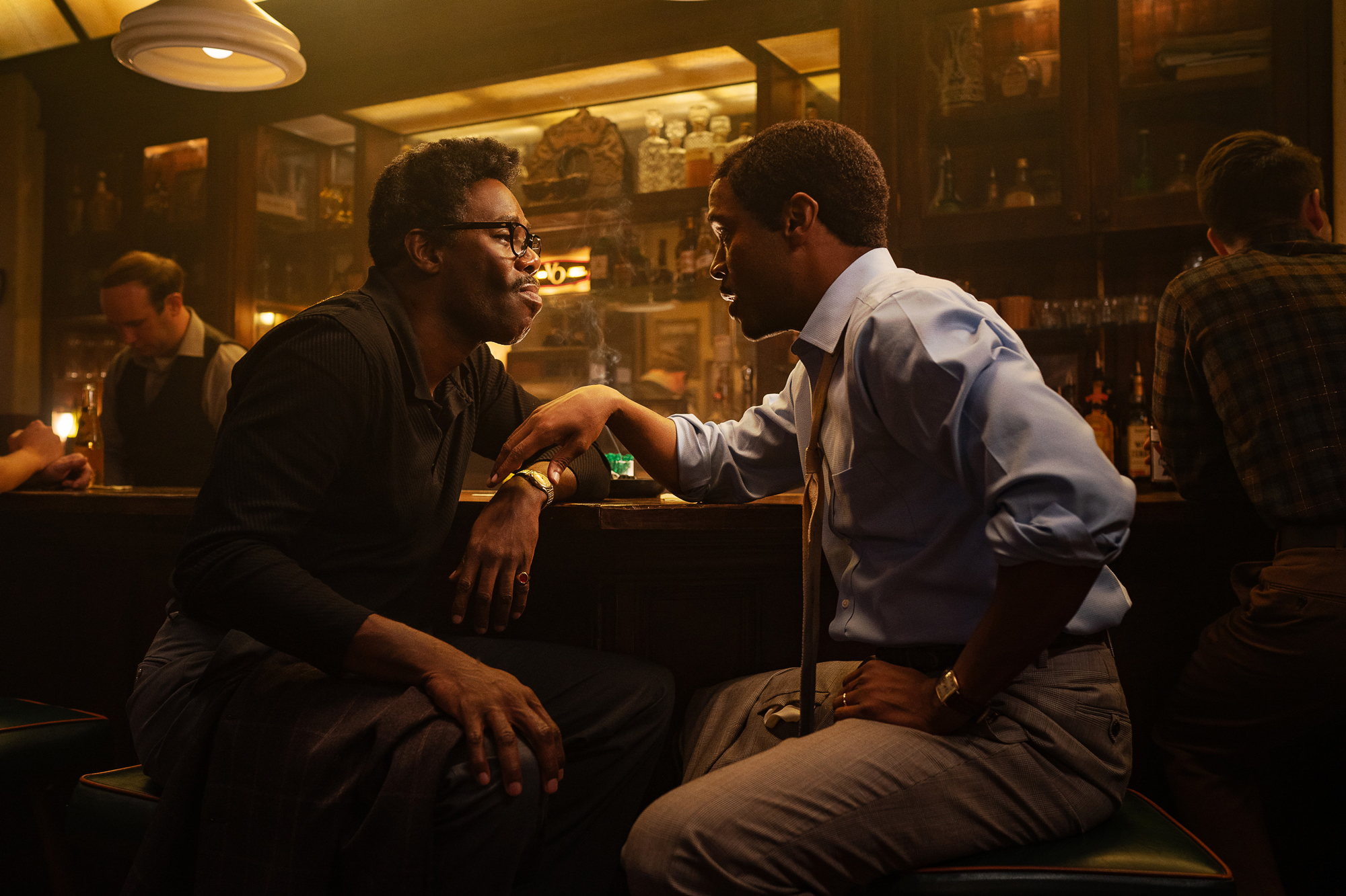 Two Black men lean towards each other while seated at bar