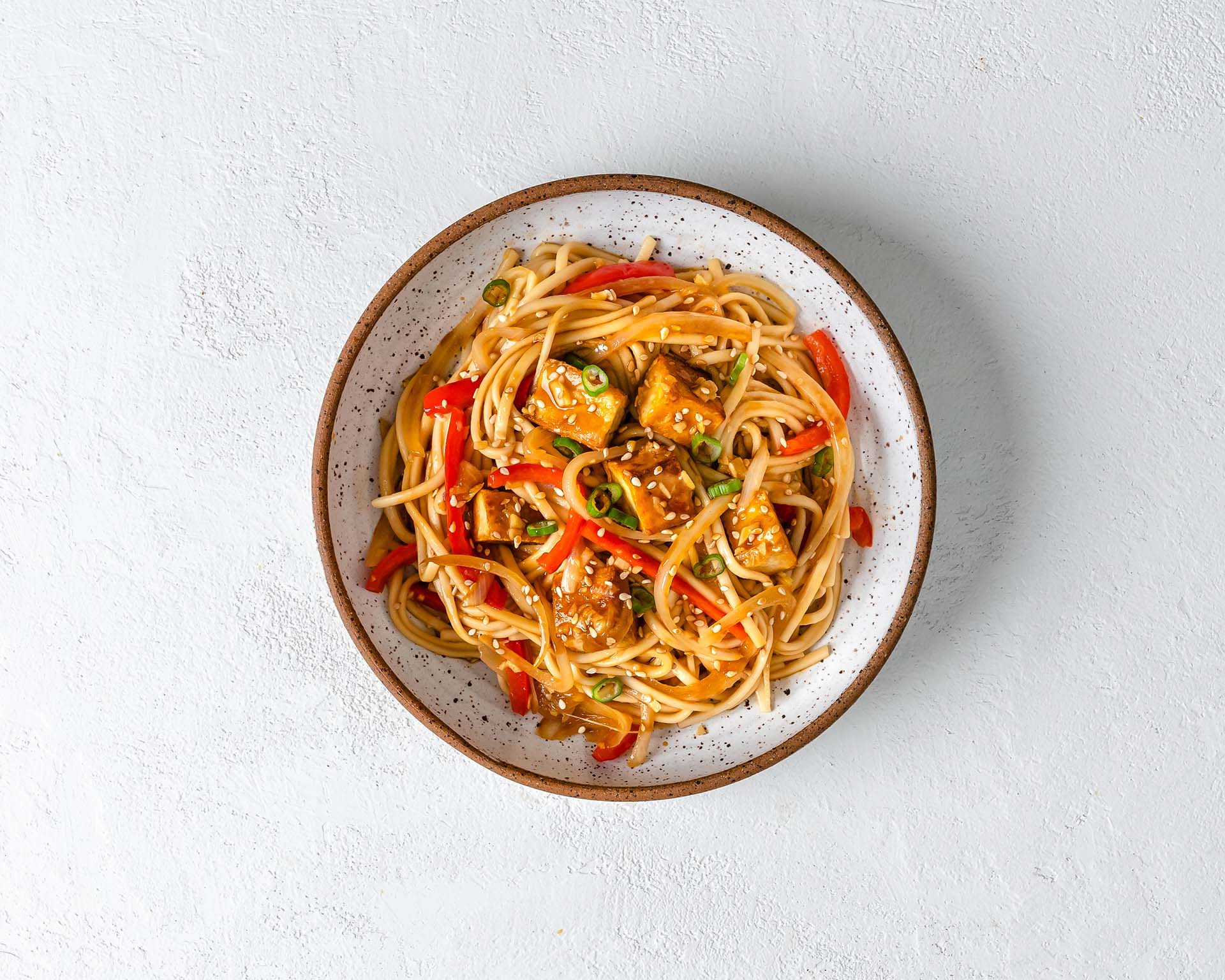 A bowl of sesame ginger noodles topped with tofu and sliced red pepper.