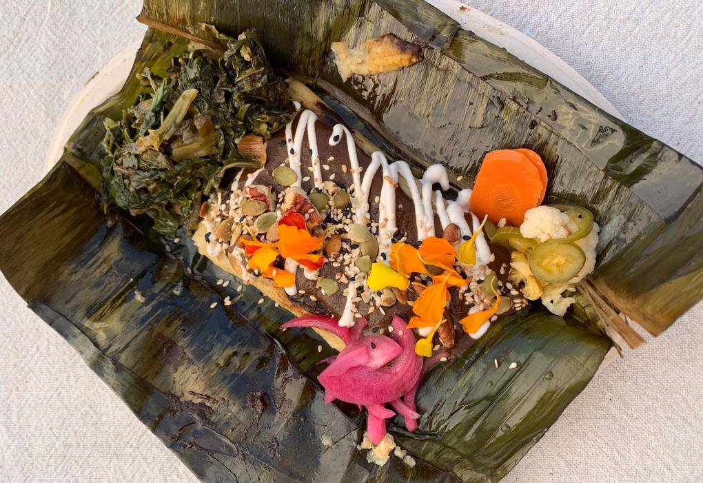 an open-faced tamale in banana leaf is decorated with a variety of colorful ingredients