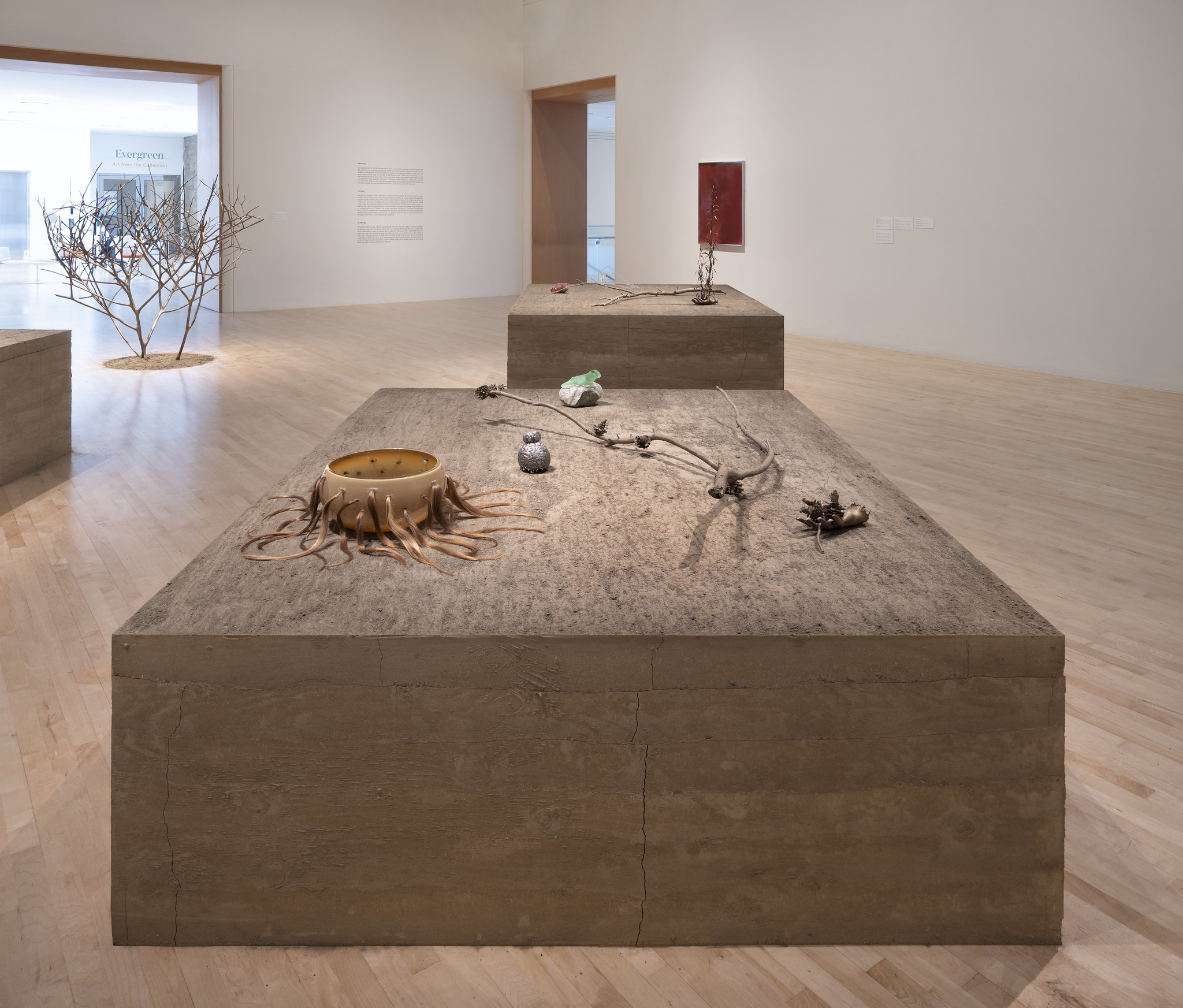 Gallery view of earthen rectangular pedestal covered in small glass and metal cast objects 