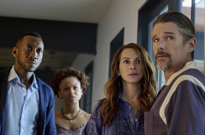 Inside a house, a middle-aged Black man stands next to a Black teenage girl. Standing slightly before them is a white woman with long brown hair and a white man with greying hair and beard. All are staring in the same direction. All look very concerned.
