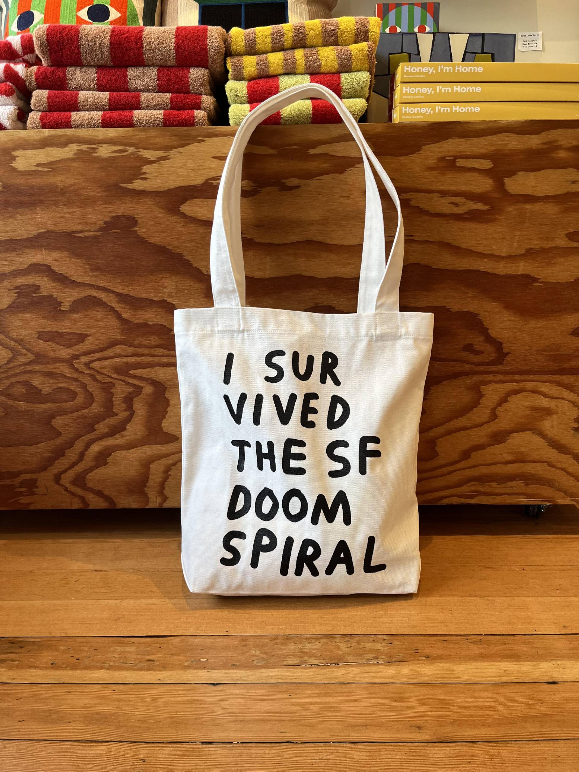White tote bag with "I survived the SF doom spiral" in black lettering