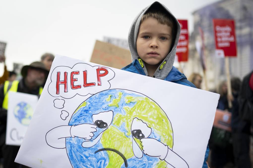 A boy holds a sign saying help during a protest for climate justice