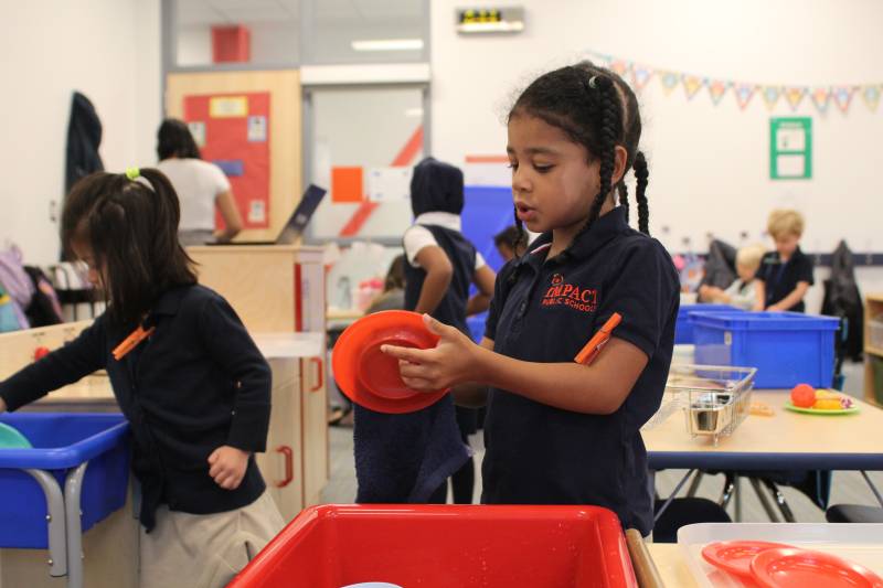 Un niño de 4 años está lavando platos como parte de una actividad en el aula.