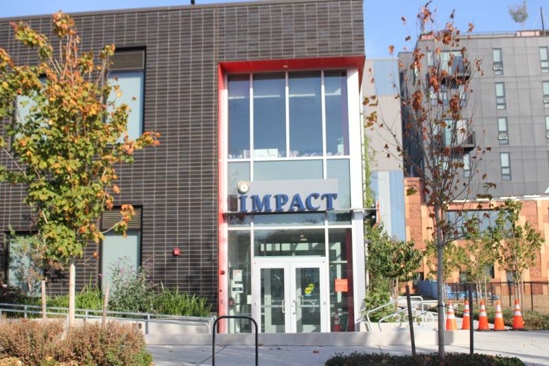 El frente del edificio de la escuela con ladrillos y ventanas.  El nombre de la escuela, Impact, está estampado sobre la entrada de doble puerta.