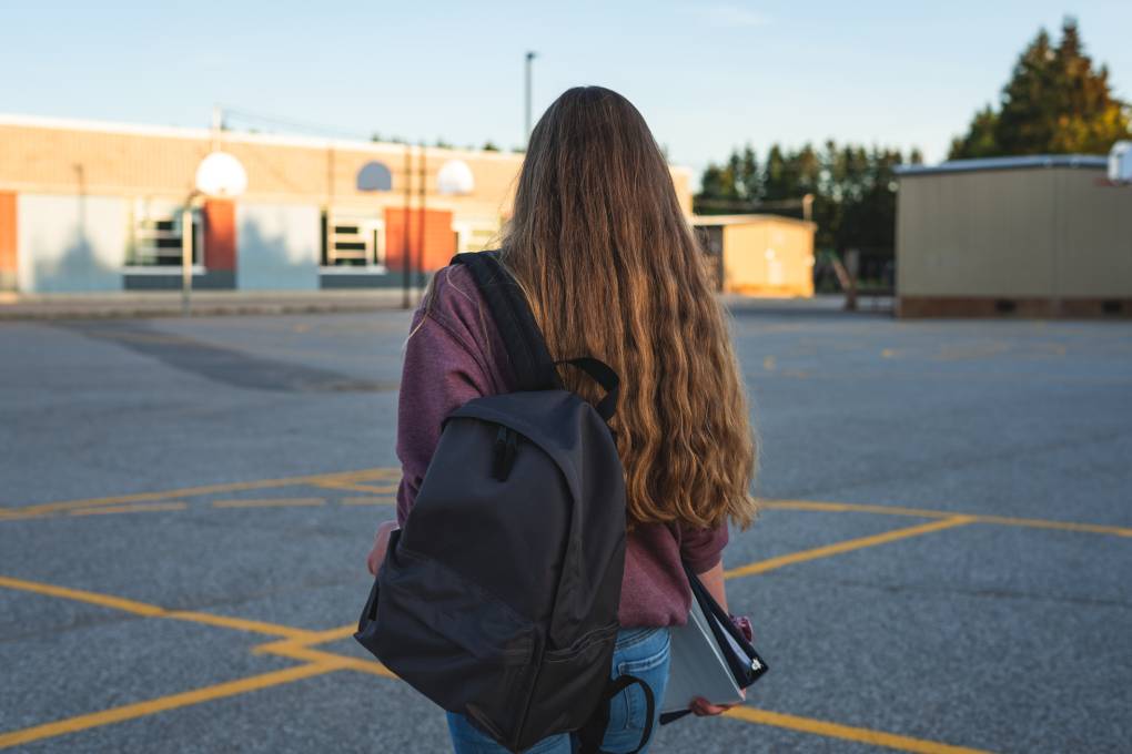 Teen girl seen from behind, at sunset in a parking lot.