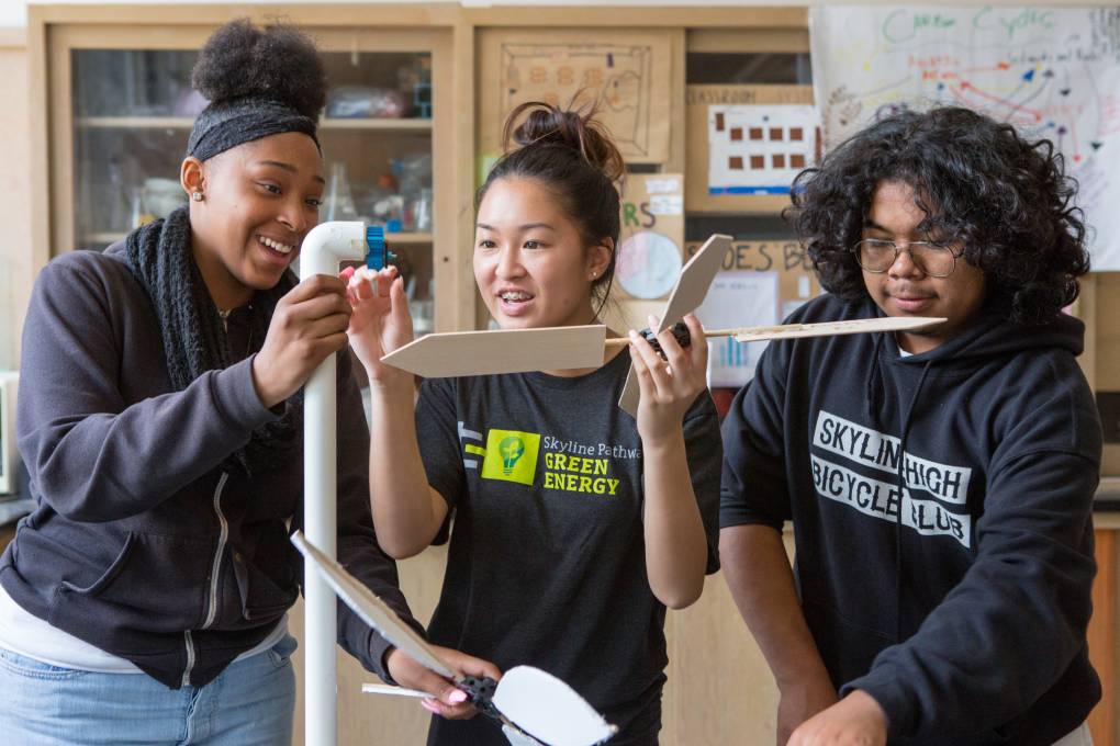 Two high school girls and one high school boy in science lab. Students assemble a model wind turbine they constructed.