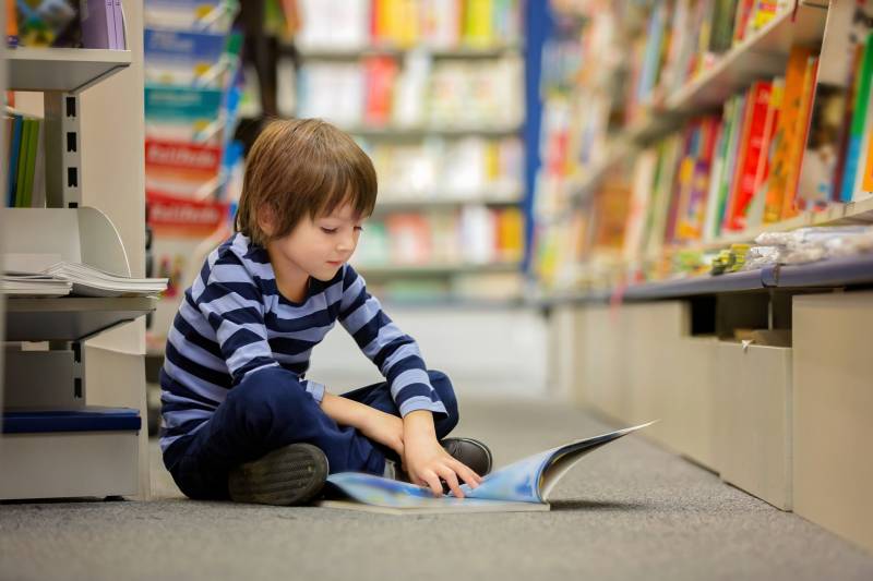 Child sits on the floor of a library reading a book