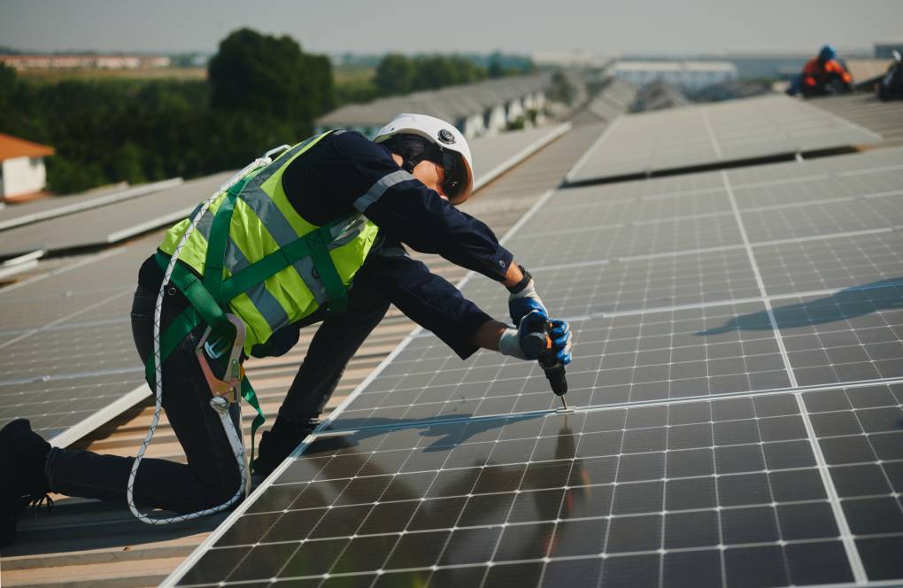 Engineer wearing protective equipment for working at height installing a solar power generation system on the roof of a factory building.