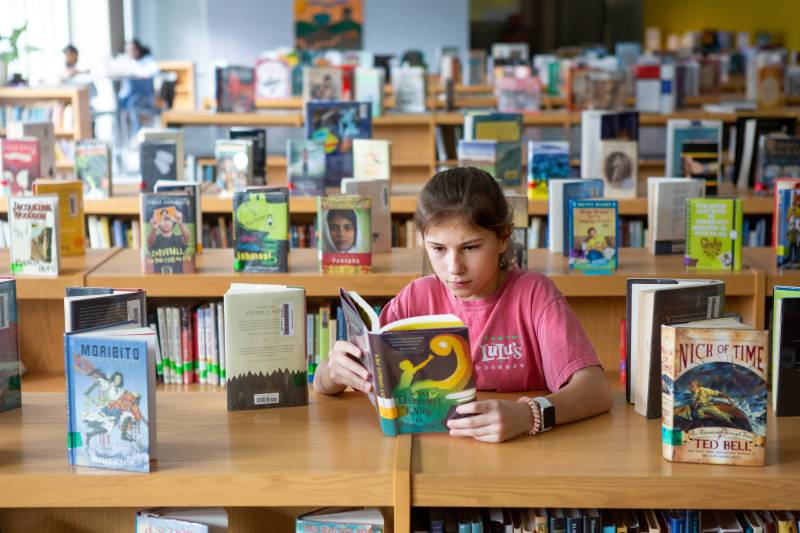 A seventh-grade student reads a book in the library stacks.