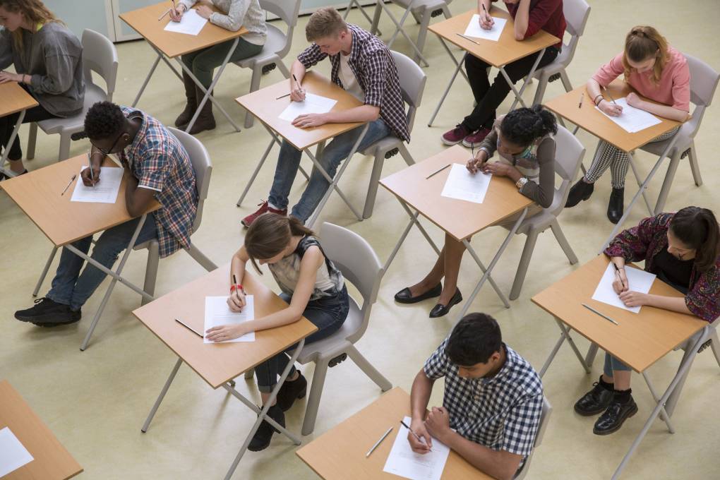 Elevated view of students writing on paper taking exam at desks