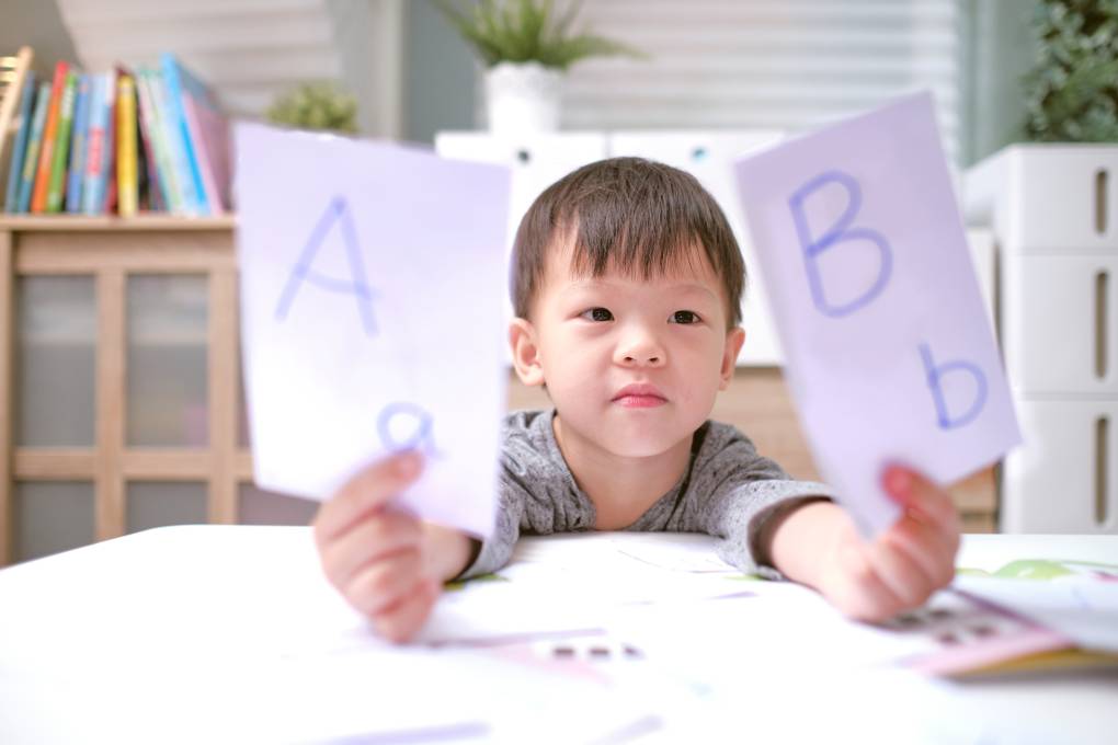 Asian or Asian American kindergarten boy holding up one flash card with a capital 'A' and lowercase 'a' and a second flash card with a capital 'B' and a lowercase 'b'