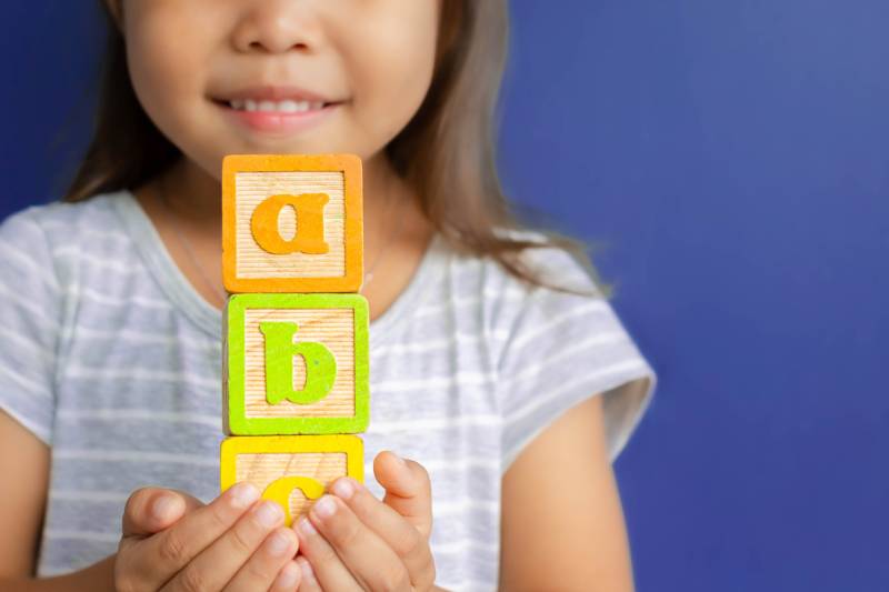 A little girl holding abc blocks infront of a blue background