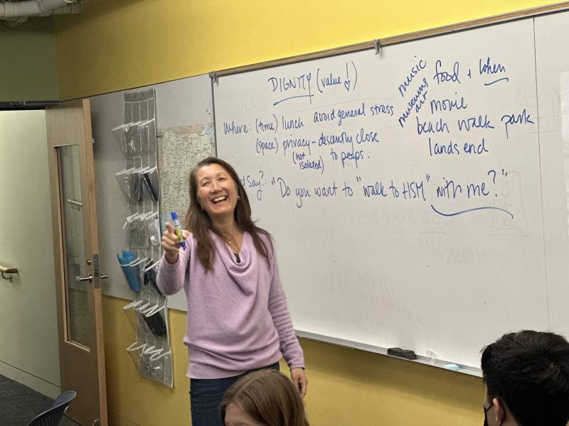 Teacher stand in front of a white board and points with a marker