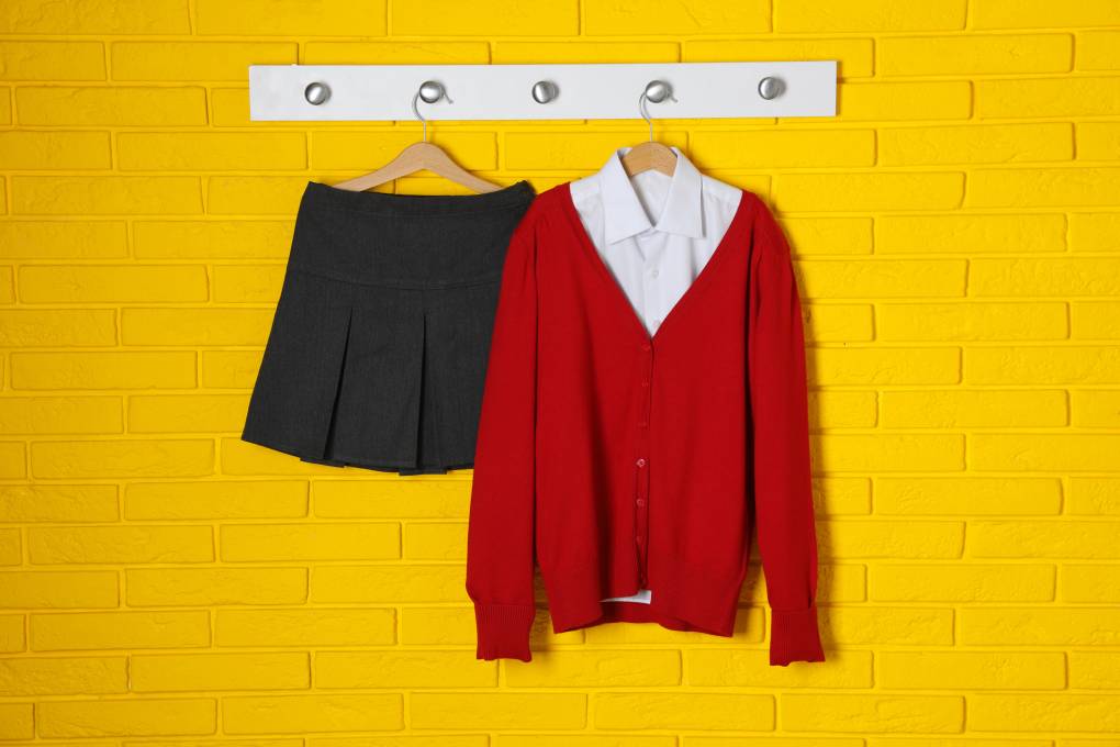 Shirt, jumper and skirt hanging on yellow brick wall. School uniform