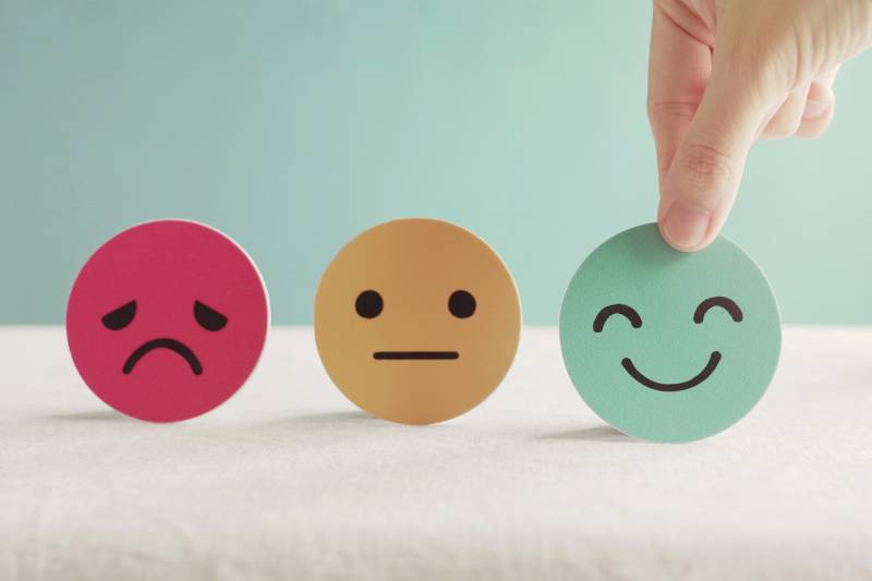 Hand choosing green happy smiley face paper next to a frown face paper and an OK face paper