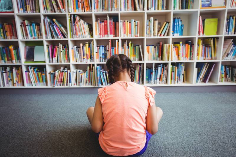 Rear view of girl reading a book in the library