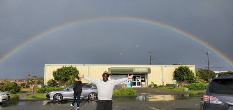 man poses in front of a rainbow