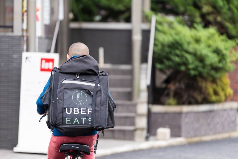 Tokyo, Japan - March 30, 2019: Shibuya street road with back of young delivery man on bicycle for uber eats