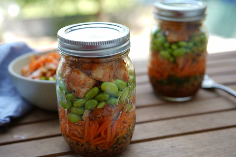 mason jars with quinoa, edamame, carrots and tofu in tem