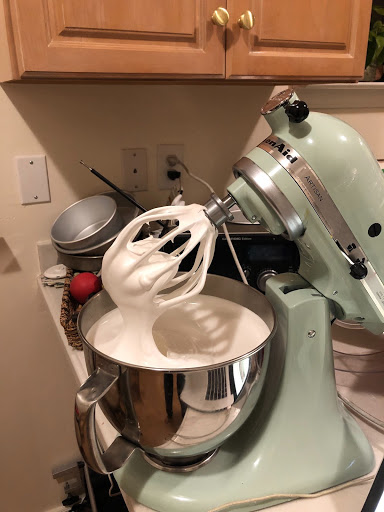 Swiss meringue buttercream in a pale blue Kitchen Aid stand mixer with the whisk attachment on and the attachment in the up position