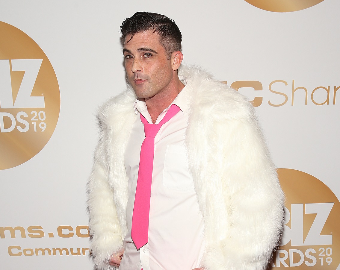 Lance Hart, an adult film performer who also runs two production companies poses in a white shirt, pink tie, and white furry coat at the 2019 XBiz Awards in Los Angeles.