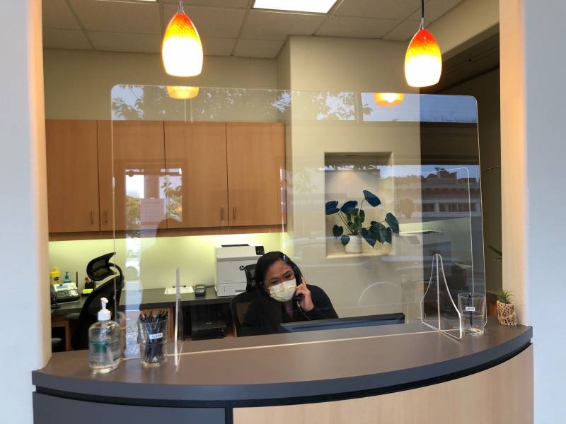 Office manager Cessalyn Maquinana at the front desk of the Better Living through Dentistry Office. New additions for the pandemic: plexiglass sneeze guards, separate cups for clean and used pens, and hand sanitizer.