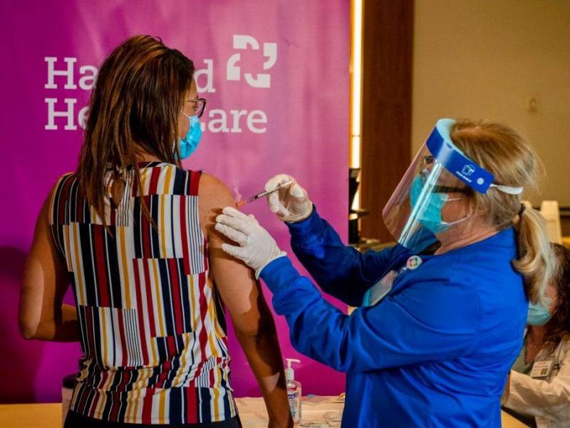 Dr. Melisha Cumberland is given the the second dose of the Pfizer/BioNTech vaccine in the arm by a medical worker wearing a face shield and a blue PPE suit.