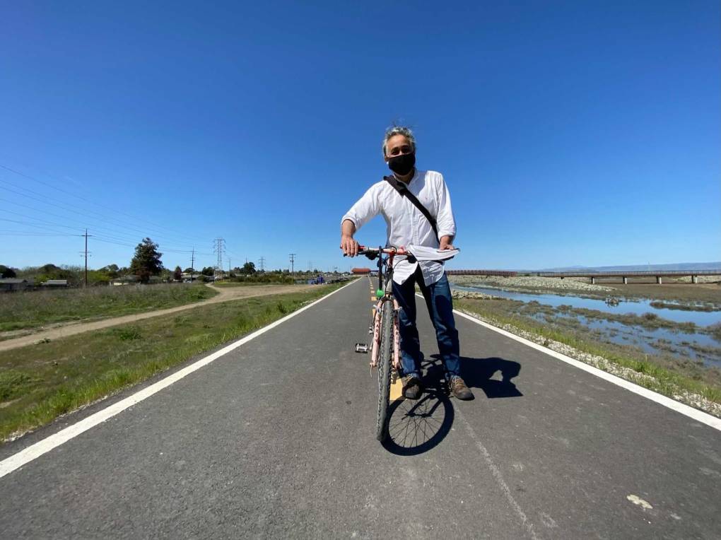 El alcalde del Este de Palo Alto, Carlos Romero, con su bicicleta en el nuevo dique que rodea partes de su ciudad. Las casas a la izquierda se encuentran a un extremo de la ciudad y a la derecha hay un arroyo que conduce a la bahía.