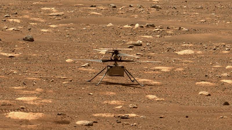 A helicopter-like machine landing on the red barren soil of Mars.