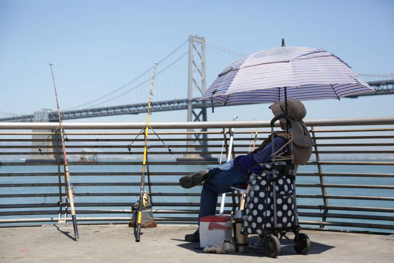 A fisherman waits under the shade of his umbrella during a heat wave.