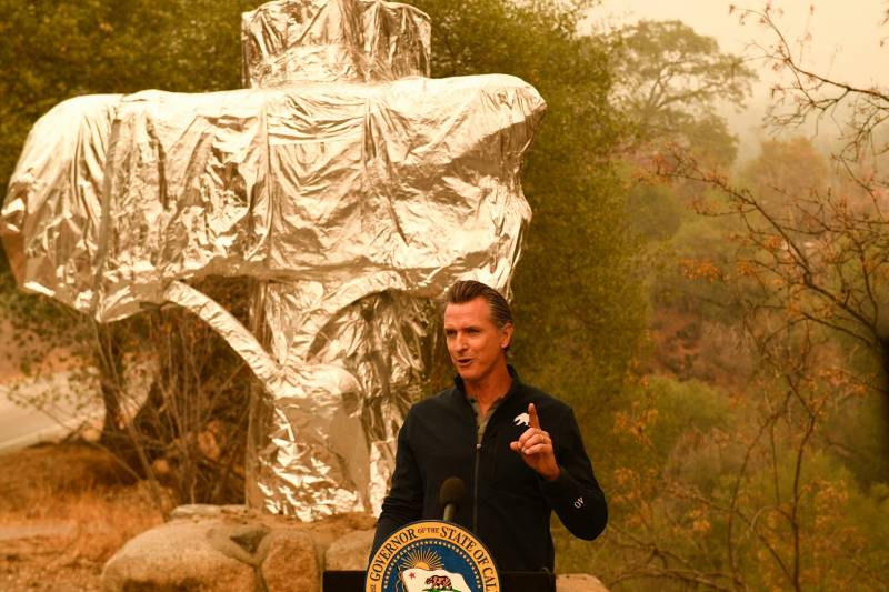 Governor Gavin Newsom speaks at a podium in a cloud of wildfire smoke.
