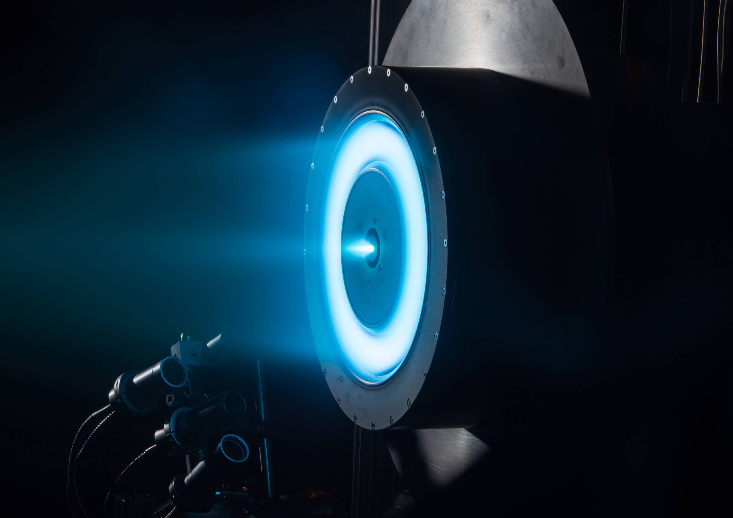 A black, round engine thruster with interior rings of bright blue. 