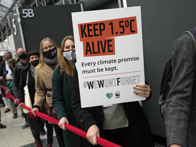 Three mask wearing climate activists grip a red velvet rope. One holds up a sign that says "keep 1.5C alive."
